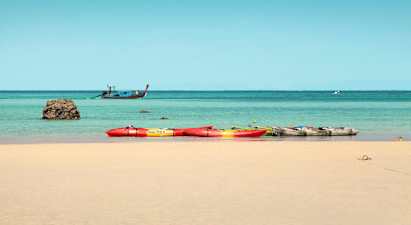 Flere kajakker på en sandstrand, med havet og en båt i bakgrunnen. (AI-generert tekst)