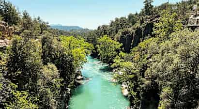 En turkisblå elv som renner gjennom en frodig ravine med klipper og trær. (AI-generert tekst)