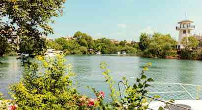 En elv med grønne busker og trær langs kantene. Et fyrtårn-lignende bygg kan ses på høyre side. (AI-generert tekst)