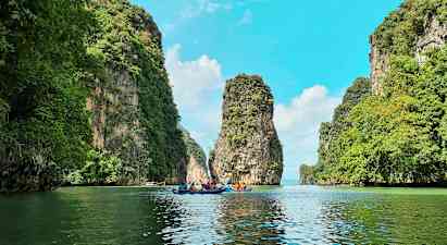 Flere personer padler kajakker gjennom en naturskjønn passasje mellom høye, grønne klipper. (AI-generert tekst)