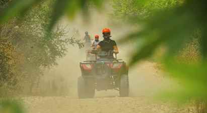 Personer som kjører firehjulinger på en støvete grusvei omgitt av vegetasjon. (AI-generert tekst)