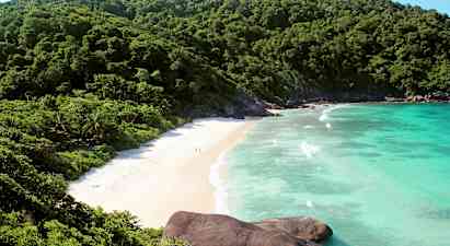 Bilde av en strand omgitt av grønne fjell og blått hav. (AI-generert tekst)