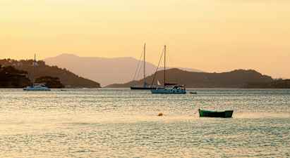 Bilde av en rolig vik ved solnedgang med seilbåter og en grønn båt i forgrunnen. (AI-generert tekst)