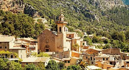 Steinkirke med tårn omgitt av en landsby blant fjell og grøntområder. (AI-generert tekst)