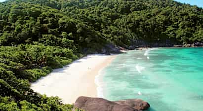 Bilde av en strand omgitt av grønne fjell og blått hav. (AI-generert tekst)
