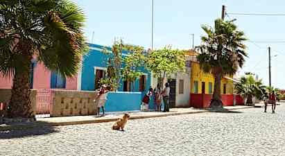 En gate med fargerike hus, palmer og mennesker som går tur. (AI-generert tekst)