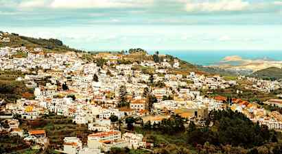 Utsikt over en by med mange hvite bygninger som ligger i en frodig dal nær havet. (AI-generert tekst)