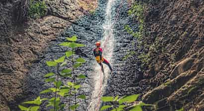 Person som rappellerer ned et fossefall med tau, omgitt av klipper og vegetasjon. (AI-generert tekst)