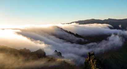 Skyer svever over en fjellkjede ved soloppgang eller solnedgang. (AI-generert tekst)
