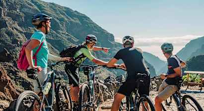 En gruppe mennesker med terrengsykler ser på en naturskjønn utsikt mellom fjell med frodige daler. (AI-generert tekst)