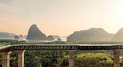 En bro med søyler leder til et område med vann og fjell i bakgrunnen. (AI-generert tekst)