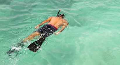 En person snorkler i klart turkisblått vann. (AI-generert tekst)