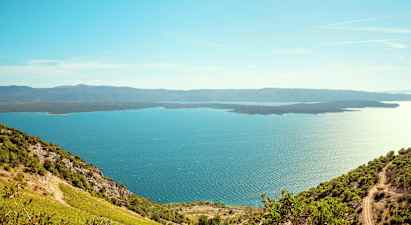 Utsikt over en blå sjø med frodige åser i forgrunnen og fjell i det fjerne. (AI-generert tekst)