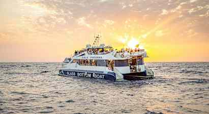 En glassbunnbåt med mennesker om bord seiler på havet under en solnedgang. (AI-generert tekst)