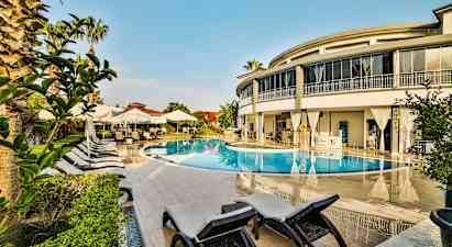 Et utendørs svømmebasseng omgitt av solsenger, parasoller og en moderne bygning. (AI-generert tekst)