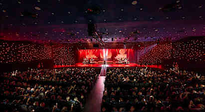 En konsertsal med en opplyst scene hvor ulike musikere opptrer foran et publikum. (AI-generert tekst)