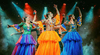 Tre personer kledd i fargerike tradisjonelle drakter danser på en opplyst scene. (AI-generert tekst)