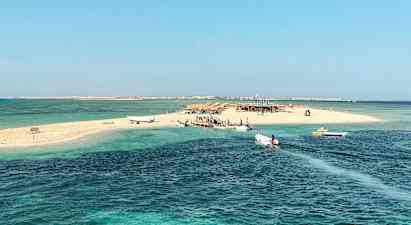 En liten sandøy med båter ved brygga, omgitt av klart blått vann. (AI-generert tekst)