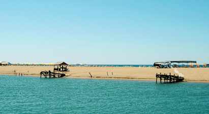 En strand ved havet med solsenger og parasoller samt en trebrygge. (AI-generert tekst)