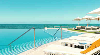 Et infinity-basseng med utsikt over havet, omgitt av solsenger og parasoller. (AI-generert tekst)