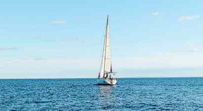 En seilbåt seiler på et åpent hav under en klar himmel. (AI-generert tekst)