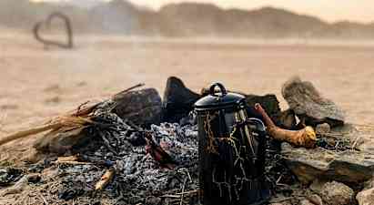 En kaffekanne står ved et utbrent bål i et ørkenlandskap. (AI-generert tekst)