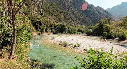 En elv med klart vann som renner gjennom et frodig landskap med fjell i bakgrunnen. (AI-generert tekst)