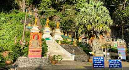 Bilde av en trapp som fører opp til flere gyldne buddhistiske statuer og strukturer omgitt av vegetasjon. (AI-generert tekst)