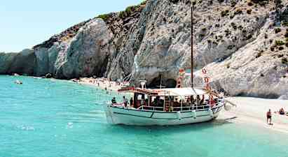En båt ligger fortøyd ved en strand med klipper og klart turkisblått vann. (AI-generert tekst)