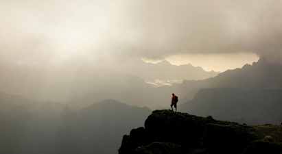 En turgåer står på en fjelltopp med tåkete daler og fjell i bakgrunnen. (AI-generert tekst)