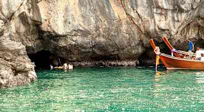 Personer svømmer i vannet ved en klippe, og to trefartøyer flyter nært. (AI-generert tekst)