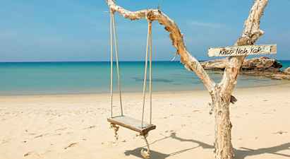 En trehus gjenna rep henger fra en gren ved stranden med blått hav i bakgrunnen. (AI-generert tekst)