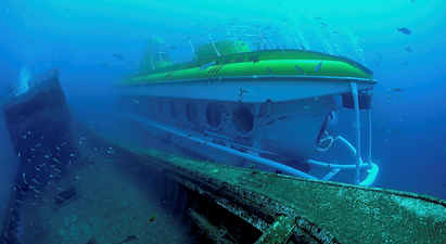 Undervannsvy av en ubåt ved siden av et gammelt skipsvrak omgitt av fisk. (AI-generert tekst)