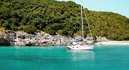 Seilbåt på turkis vann nær en frodig strand. (AI-generert tekst)