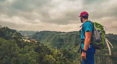 En person med ryggsekk står og ser ut over en grønn dal under overskyet vær. (AI-generert tekst)