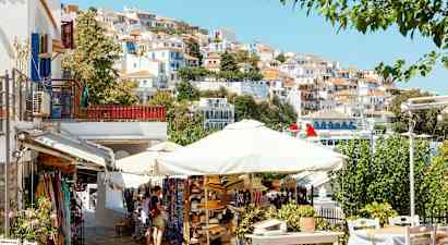 En pittoresk by med hvite hus med rødt tak på en skråning, parasoller og salgsboder i forgrunnen. (AI-generert tekst)