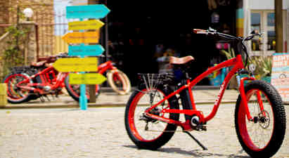 Rød sykkel på brosteinsunderlag med fargerike veiskilt i bakgrunnen. (AI-generert tekst)