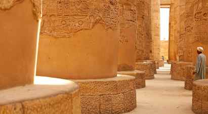 Steinsøyler med hieroglyfer i en historisk bygning, en person står nær. (AI-generert tekst)