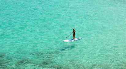 Person som padler stående på en paddleboard i klart turkis vann. (AI-generert tekst)