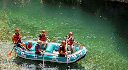 En gruppe mennesker driver med rafting i en oppblåsbar flåte på klart vann, og har på seg hjelmer og redningsvester. (AI-generert tekst)