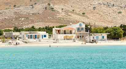 Bilde av en klarblå bukt med en sandstrand som har hus og åser i bakgrunnen. (AI-generert tekst)