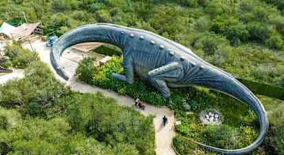 En stor dinosaurstatue omgitt av grønt sett ovenfra. (AI-generert tekst)