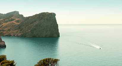 En klippe ved en kyst med en båt som kjører på vannet. (AI-generert tekst)