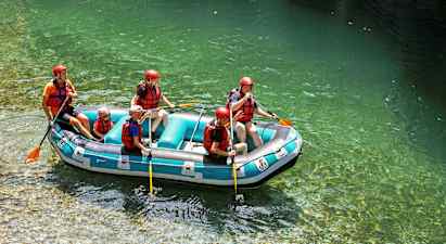 En gruppe mennesker driver med rafting i en oppblåsbar flåte på klart vann, og har på seg hjelmer og redningsvester. (AI-generert tekst)