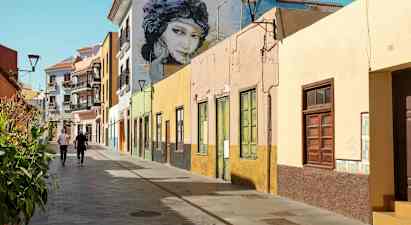 Fargerike husfasader langs en gangvei med to personer som går. (AI-generert tekst)