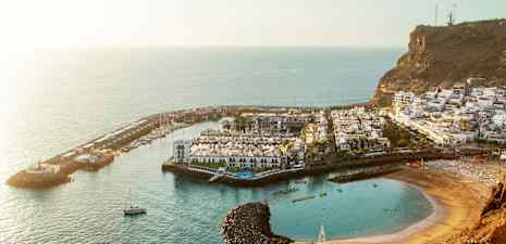 En kystby med en båthavn, hvite bygninger og en strand omgitt av klipper. (AI-generert tekst)