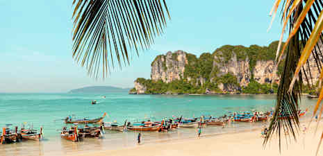 En strand med longtailbåter og klipper ved sjøen. (AI-generert tekst)