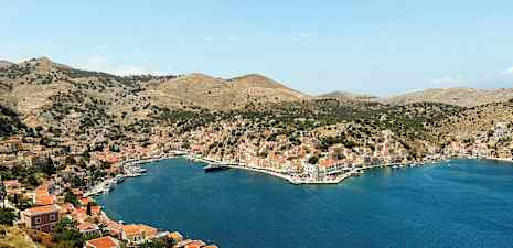 Bilde av en bukt omgitt av åser med hus og småbåter ved vannet. (AI-generert tekst)