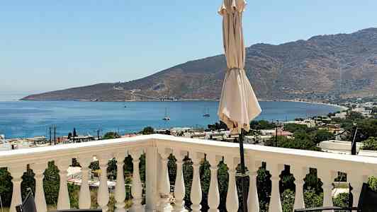 En utsikt fra en terrasse med rekkverk, en parasoll og havet og fjell i bakgrunnen. (AI-generert tekst)