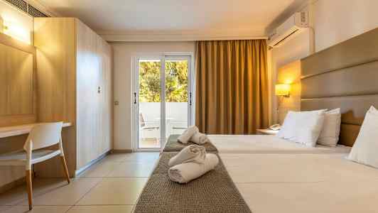 Et hotellrom med to enkeltsenger, skrivebord og en glassdør som fører til en balkong. (AI-generert tekst)